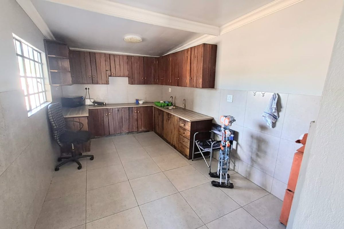 A functional office kitchenette featuring wooden cabinetry, tiled flooring, and a stainless steel sink, providing essential utility space for the workplace.