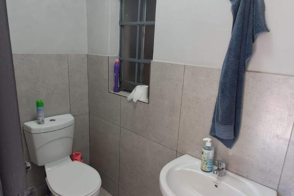 A compact office restroom featuring a pedestal basin, a standard toilet, and neutral wall and floor tiling.
