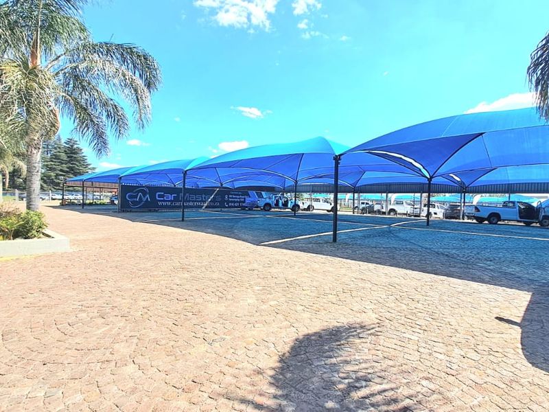 Outdoor parking area featuring extensive blue shade cloth structures over paved ground, suitable for commercial vehicle display or staff parking.