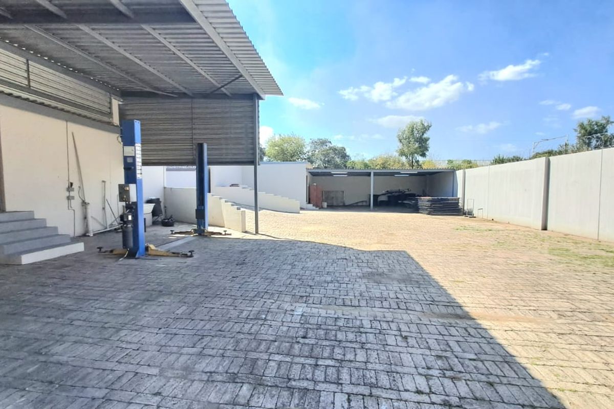 Spacious outdoor yard area featuring paved surfaces, a covered workshop section with vehicle lifts, and perimeter walling.