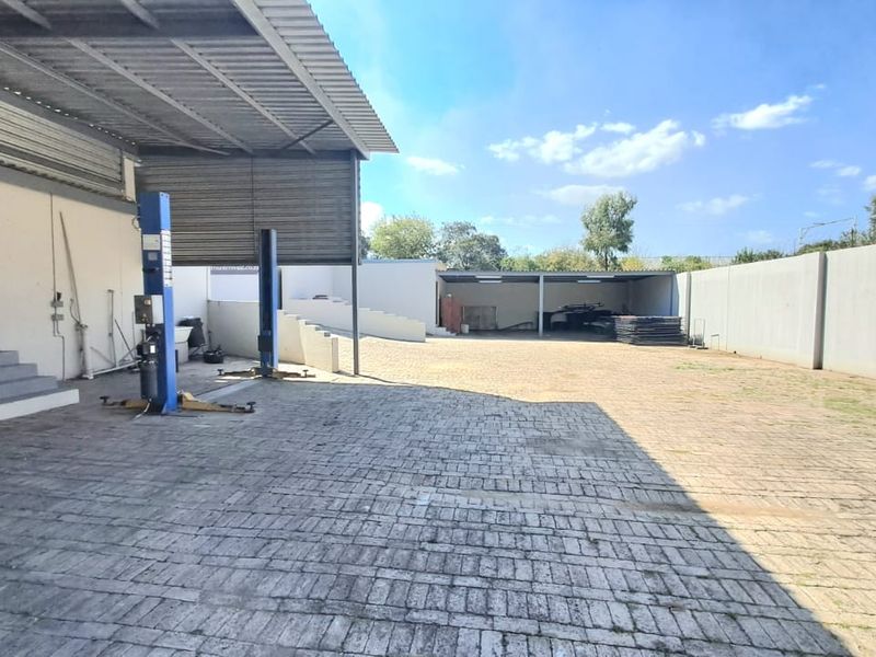 Spacious outdoor yard area featuring paved surfaces, a covered workshop section with vehicle lifts, and perimeter walling.