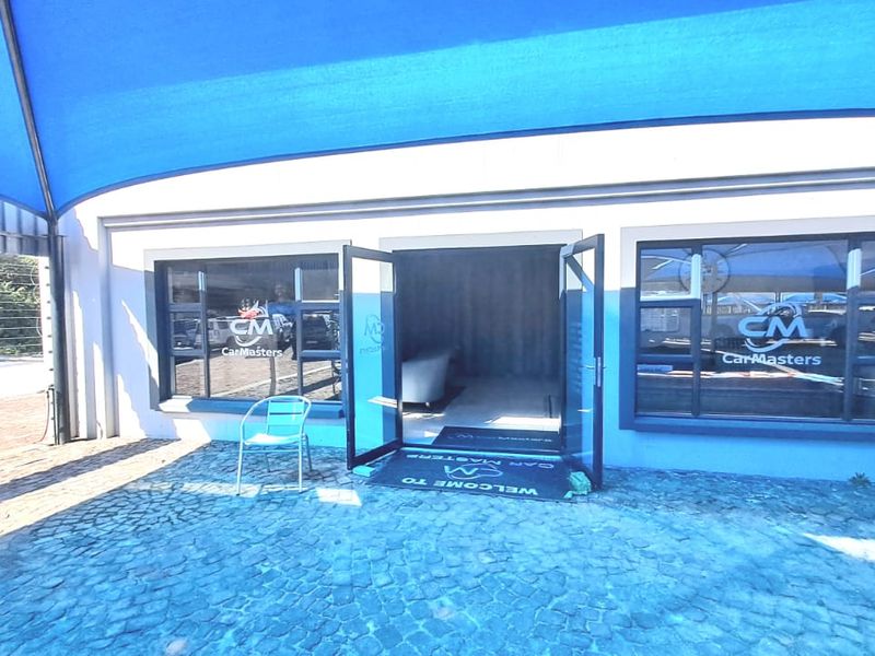 Exterior view of an office entrance featuring large glass windows, double glass doors, and a blue shade sail covering the paved entrance area.