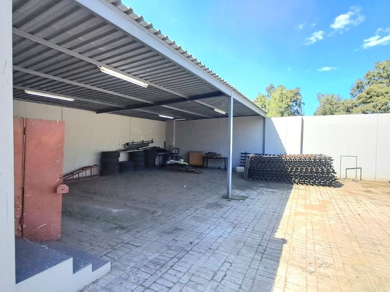 A spacious covered outdoor utility or storage area featuring a corrugated metal roof, paved flooring, and perimeter walling, suitable for various commercial storage needs.