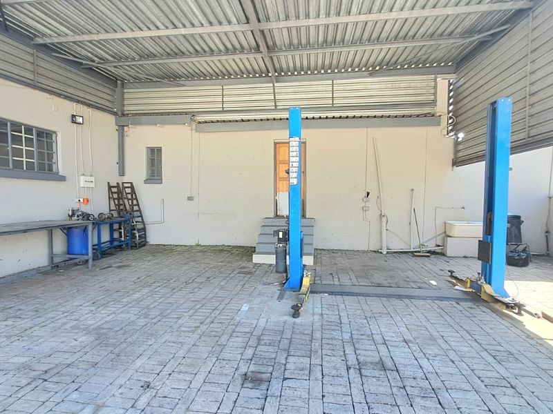 A functional workshop or garage space featuring a two-post vehicle lift, concrete block paving, and a covered roof structure.