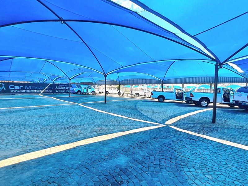 Large paved outdoor parking area featuring extensive blue shade cloth canopy structures for vehicle protection.