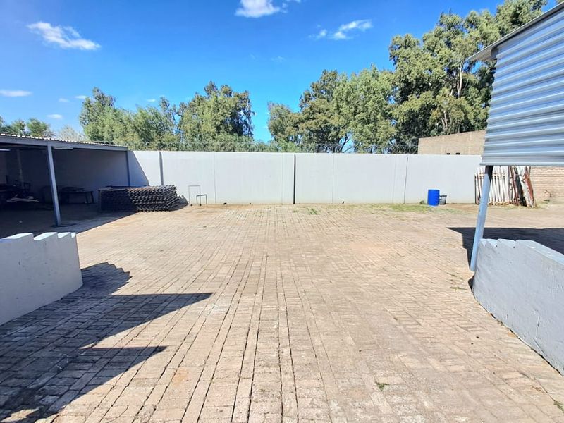 A spacious outdoor yard area featuring paved ground, perimeter walling, and covered storage or workspace structures.