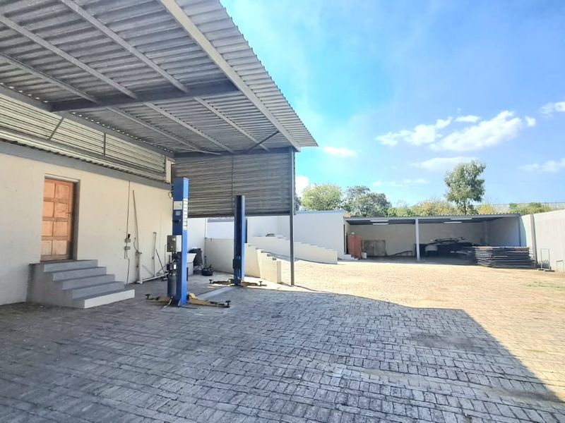 Spacious outdoor industrial yard featuring a covered work area, vehicle lift, and paved surface, suitable for automotive or storage operations.