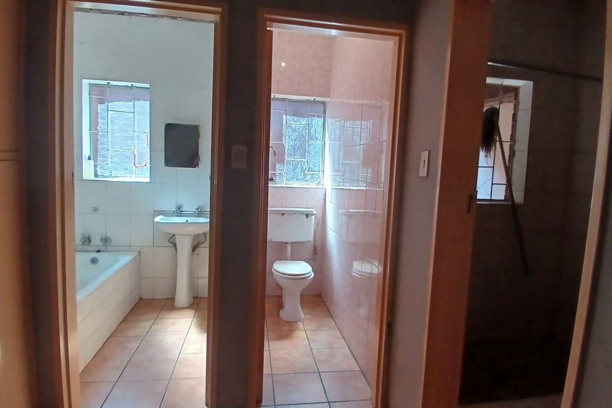 A view into a dated bathroom suite featuring a bathtub, pedestal basin, and separate toilet area with original tiling.