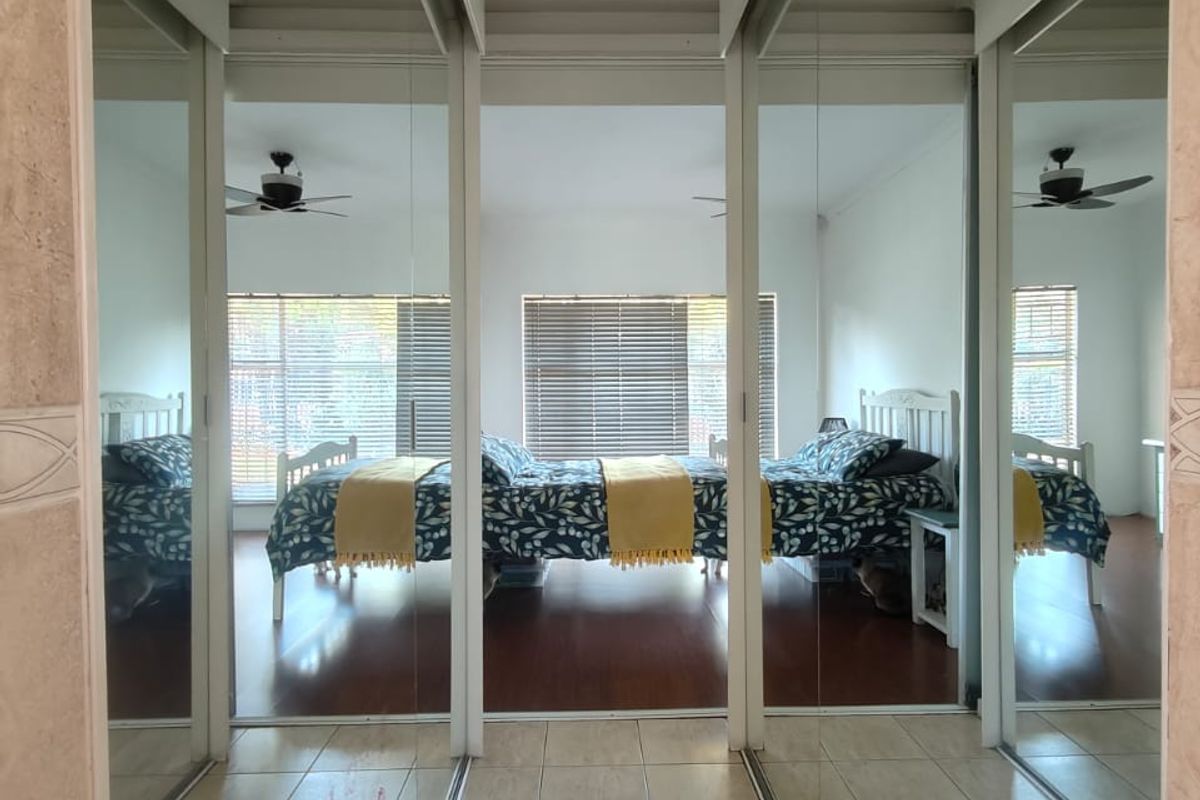 A bedroom view through a hallway featuring floor-to-ceiling mirrored sliding wardrobe doors, tiled flooring, and a ceiling fan.