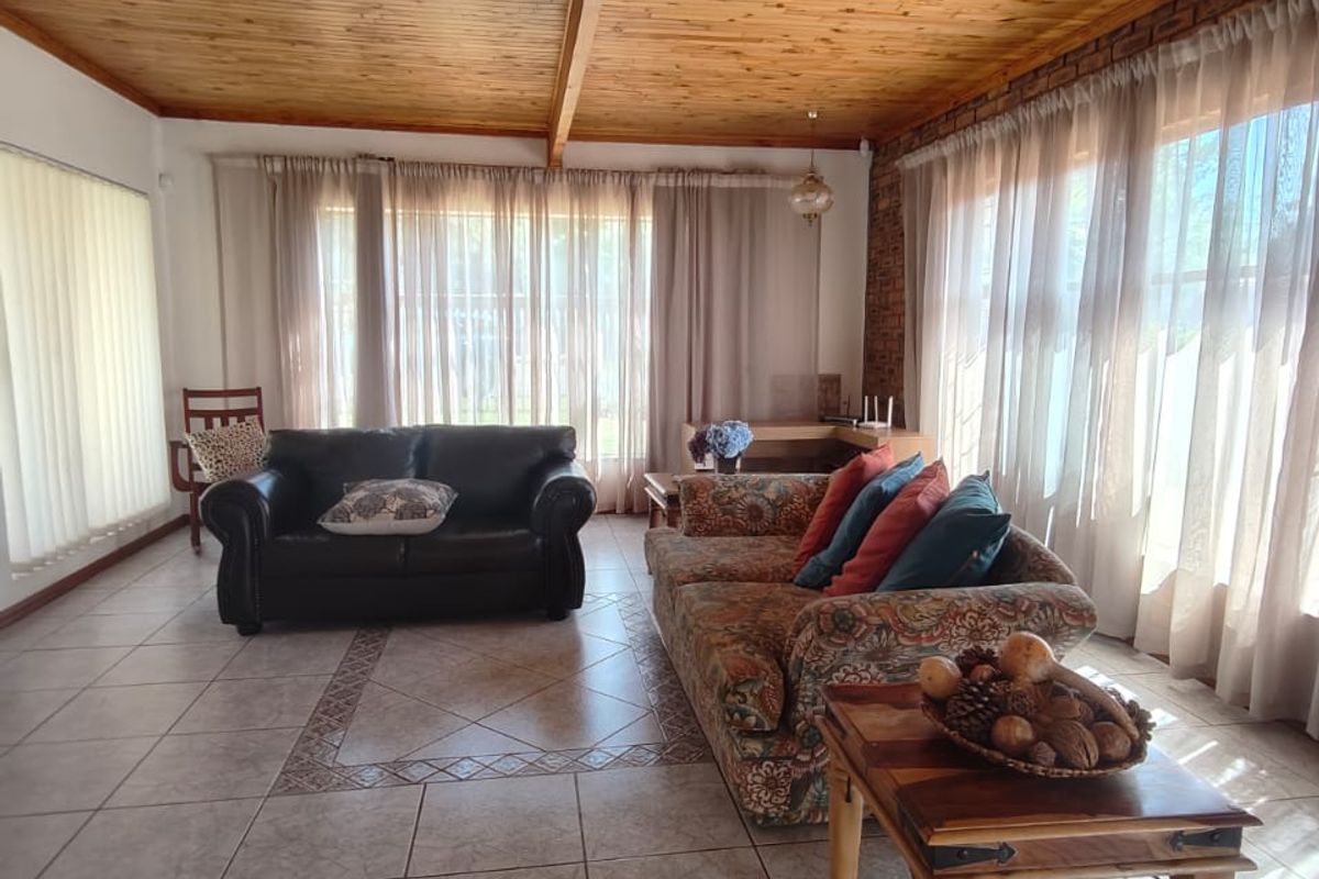 Spacious living room featuring a high timber-clad vaulted ceiling, tiled flooring, and large windows allowing for abundant natural light.