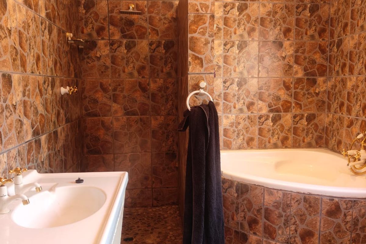 A dated bathroom featuring a corner bathtub, a walk-in shower enclosure, and a vanity basin with stone-effect wall and floor tiling.