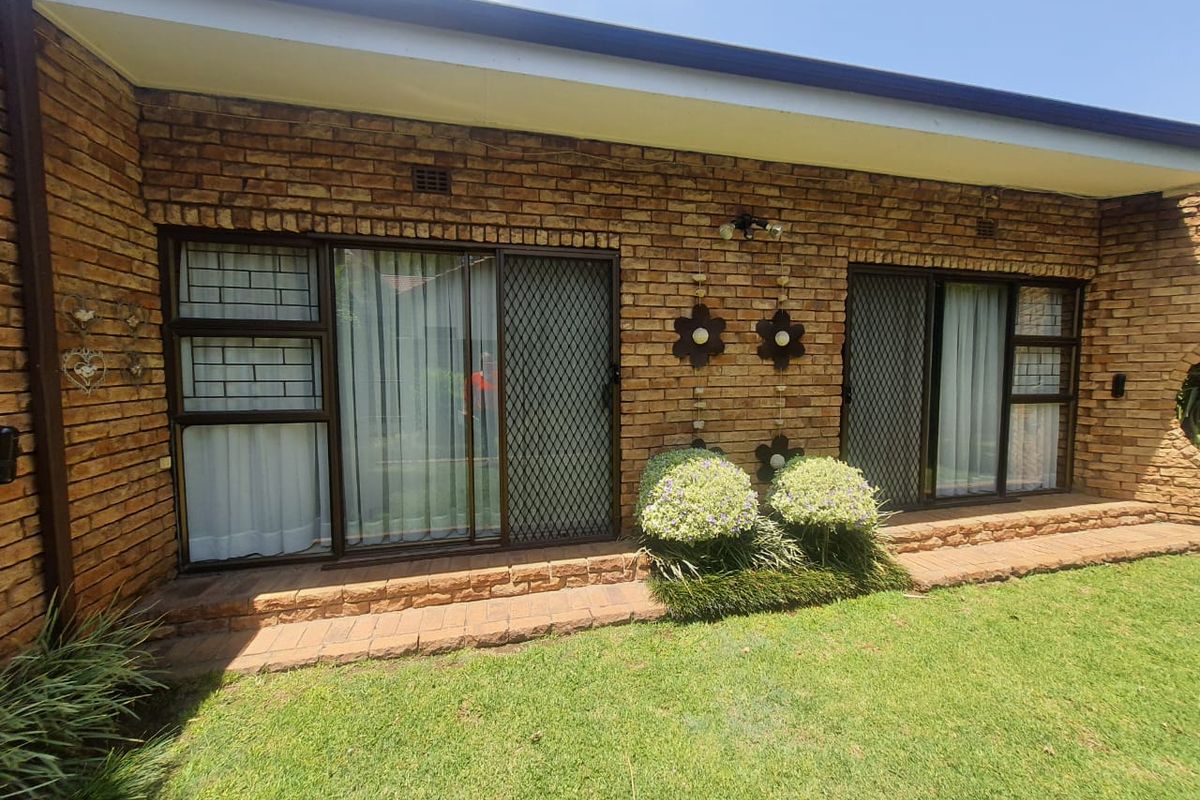 A rear exterior view of the house featuring face-brick walls, sliding glass doors with security screens, and a paved walkway leading to the garden.