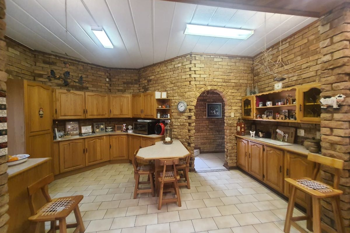 Spacious kitchen featuring rustic face-brick walls, timber cabinetry, tiled flooring, and a central breakfast nook with an arched entryway.
