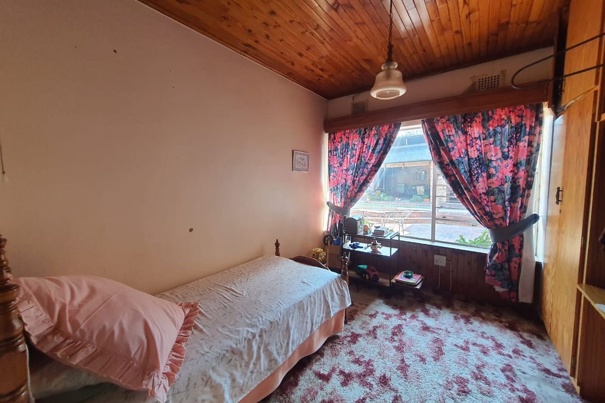 A bedroom featuring a timber tongue and groove ceiling, built-in wardrobe, and large window with garden views.