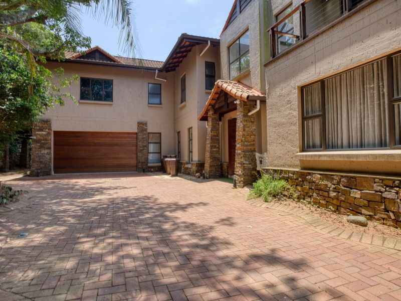 Front elevation of a multi-story residence featuring a paved driveway, stone-clad accents, and a timber garage door.