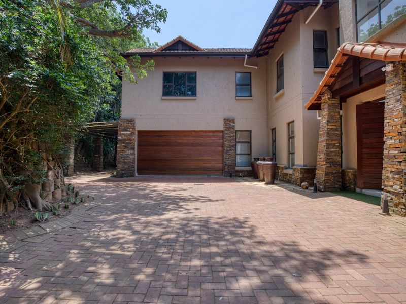 Front elevation of a double-story house featuring a paved driveway, stone-clad accents, and a wooden garage door.