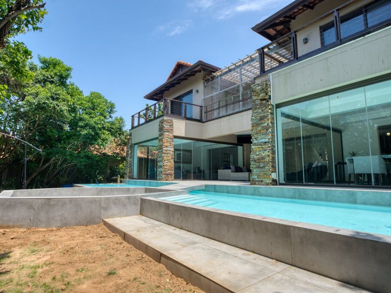 Modern multi-level residence featuring a contemporary swimming pool, stone-clad pillars, and expansive glass sliding doors opening to the outdoor living area.
