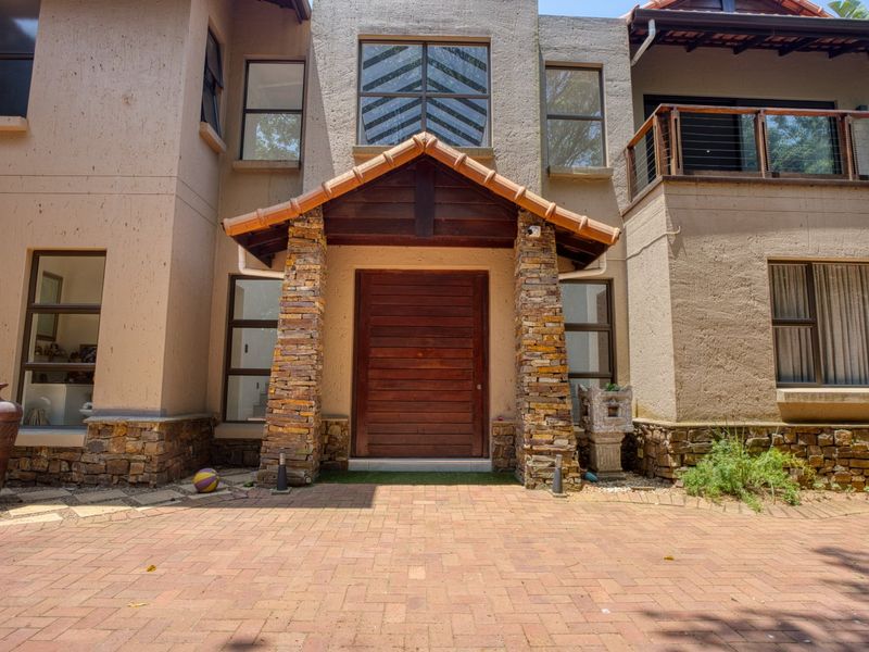 Front facade of a multi-story house featuring stone cladding, a prominent timber entrance door, and a paved driveway.