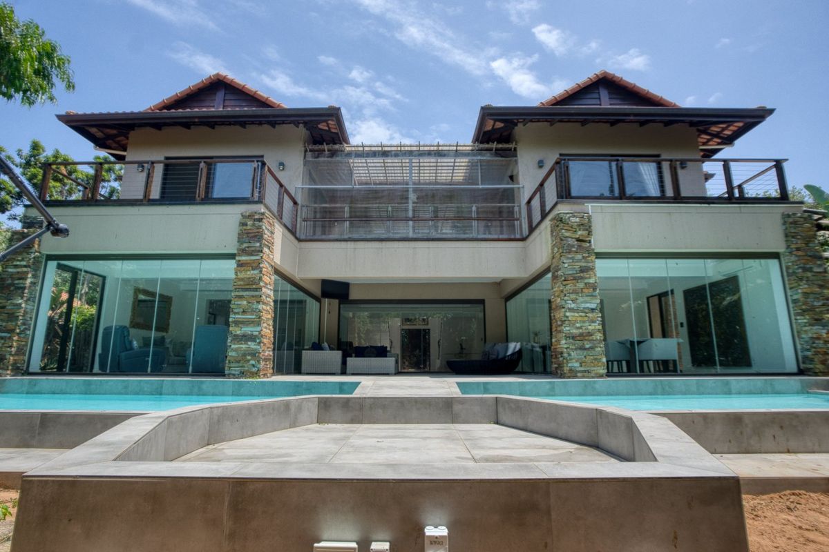 Rear elevation of a modern double-story house featuring a swimming pool, stone-clad pillars, expansive glass sliding doors, and an upper-level balcony.