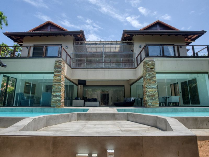 Rear elevation of a modern double-story house featuring a swimming pool, stone-clad pillars, expansive glass sliding doors, and an upper-level balcony.