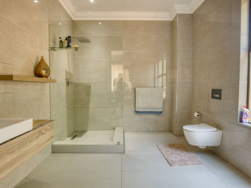 Modern bathroom featuring a walk-in shower with glass screen, wall-mounted toilet, and floating vanity with neutral floor-to-ceiling tiling.