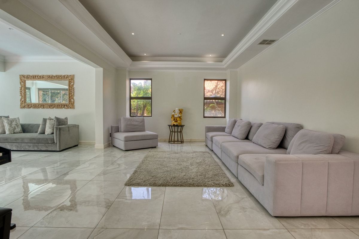 Spacious living area featuring polished porcelain floor tiles, recessed tray ceiling with cove lighting, and large windows providing natural light.