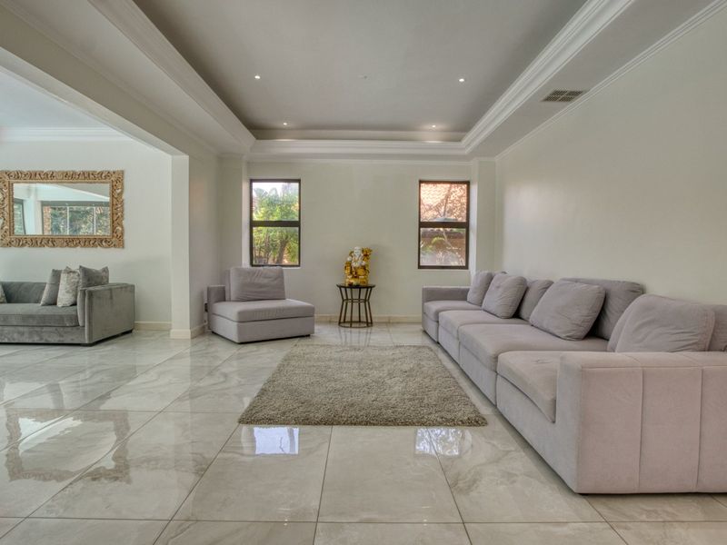 Spacious living area featuring polished porcelain floor tiles, recessed tray ceiling with cove lighting, and large windows providing natural light.