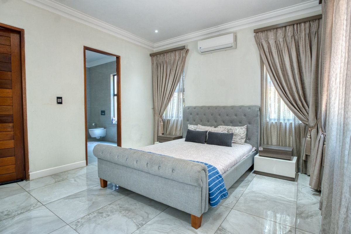 A well-maintained bedroom featuring large format floor tiles, crown molding, and an integrated air conditioning unit, with direct access to an en-suite bathroom.