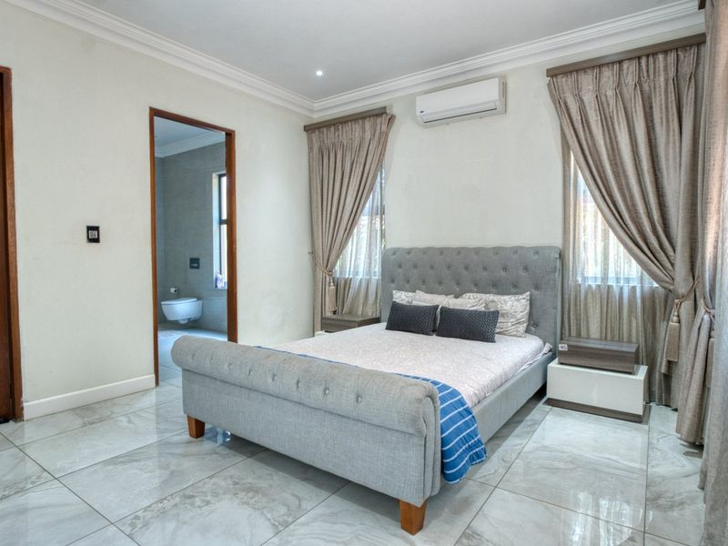 A well-maintained bedroom featuring large format floor tiles, crown molding, and an integrated air conditioning unit, with direct access to an en-suite bathroom.