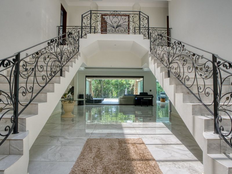 Grand entrance hall featuring a symmetrical staircase with ornate wrought iron balustrades, polished marble flooring, and expansive views through large sliding glass doors.