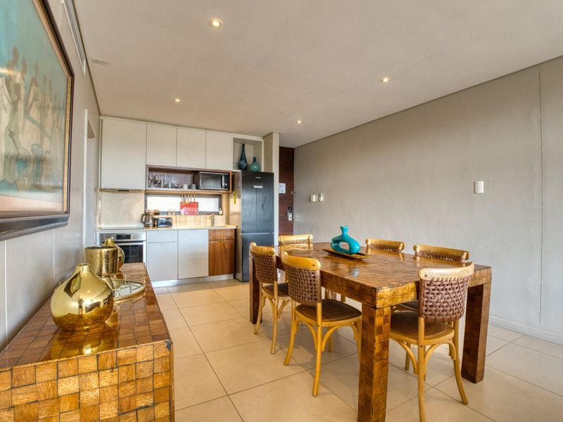 An open-plan living and dining area featuring a compact kitchen with modern cabinetry, integrated appliances, and neutral tiled flooring throughout.