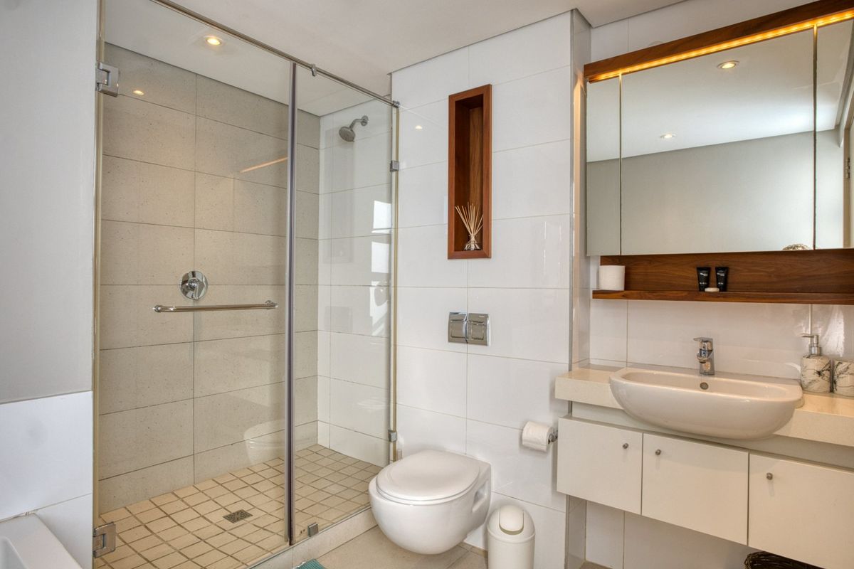 Modern bathroom featuring a glass-enclosed shower, wall-mounted toilet, sleek vanity with integrated sink, and a built-in mirrored medicine cabinet with warm accent lighting.