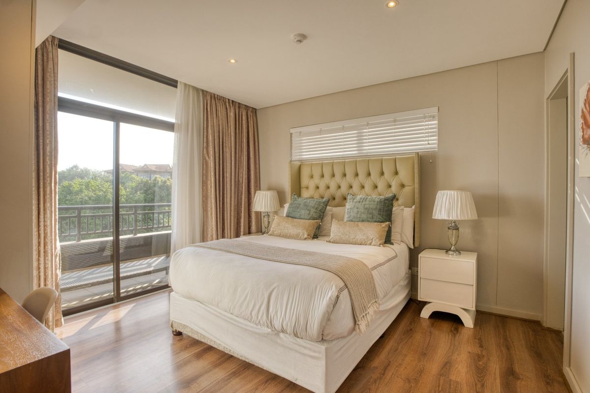 A well-lit bedroom featuring laminate flooring, recessed lighting, and a large sliding glass door providing access to an outdoor balcony.