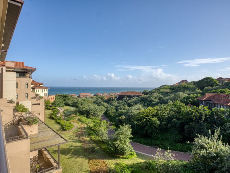 Elevated view overlooking a lush green estate, paved pathways, and the ocean in the distance from a private balcony.