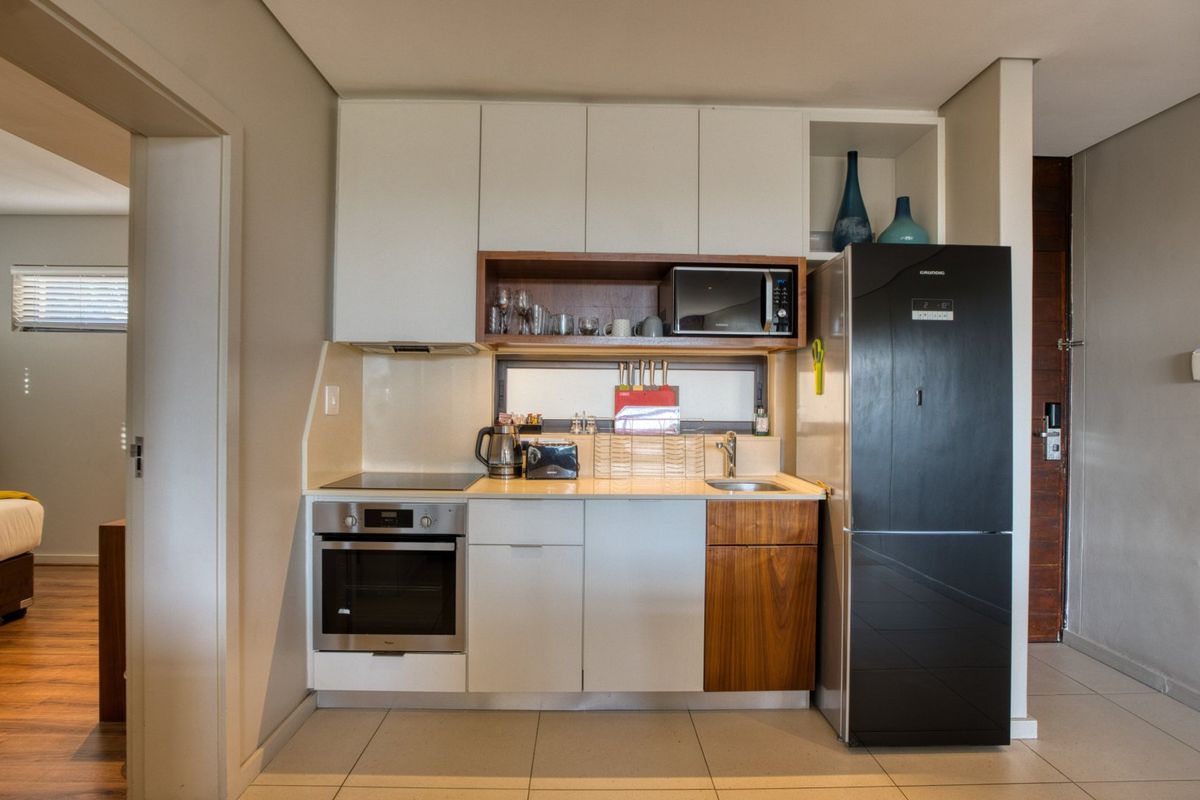 Compact modern kitchen featuring built-in cabinetry, integrated oven and hob, stainless steel sink, and sleek finishes.