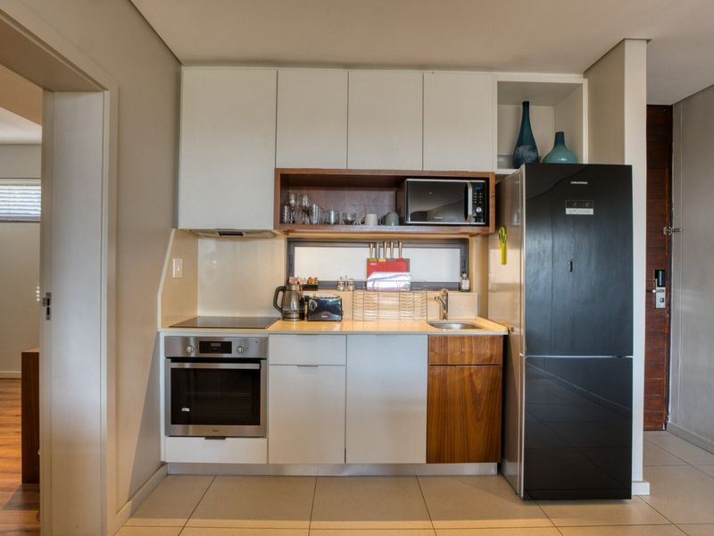 Compact modern kitchen featuring built-in cabinetry, integrated oven and hob, stainless steel sink, and sleek finishes.