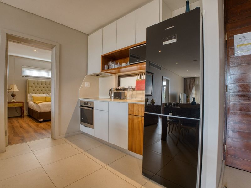 Compact modern kitchen featuring sleek white and wood-tone cabinetry, integrated appliances, and tiled flooring, with direct access to the bedroom.