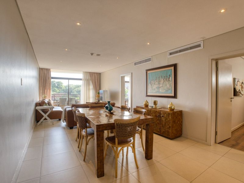 Spacious open-plan living and dining area featuring neutral tiled flooring, recessed lighting, and direct access to a private balcony through sliding glass doors.