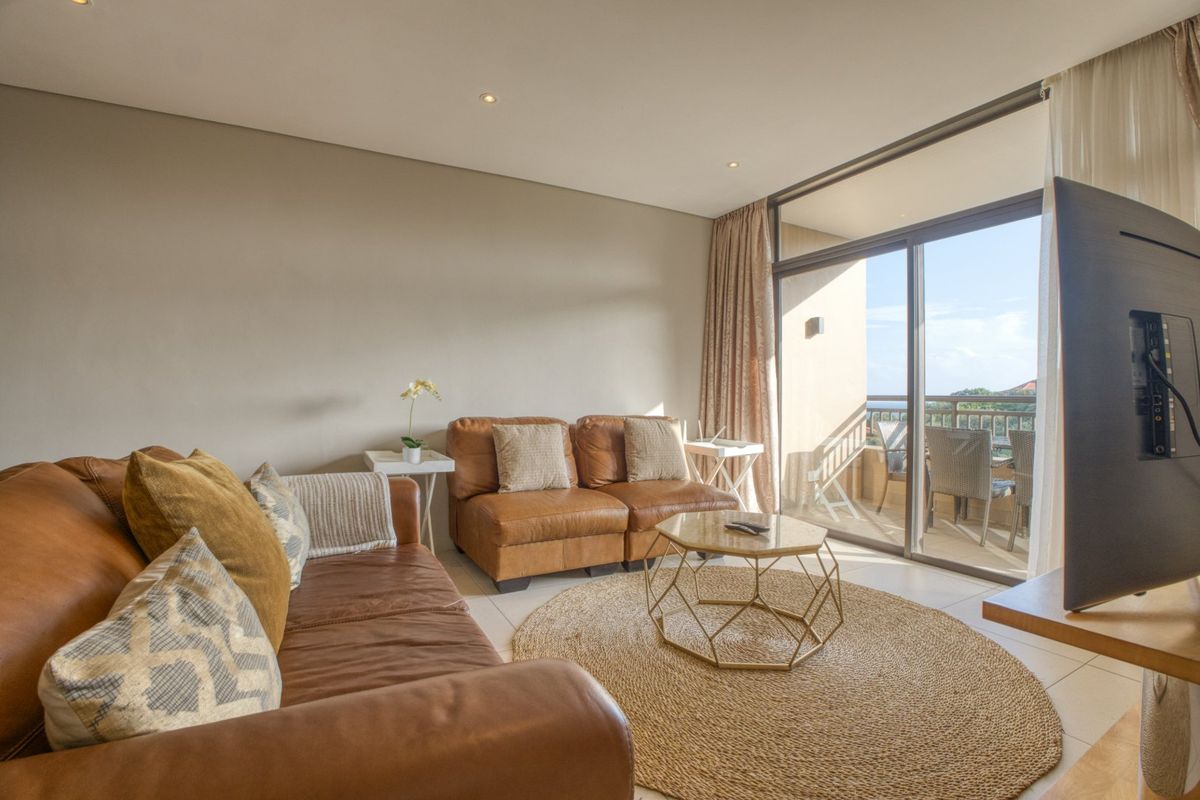 A bright living room featuring tiled flooring, recessed downlights, and large sliding glass doors providing direct access to an outdoor balcony area.