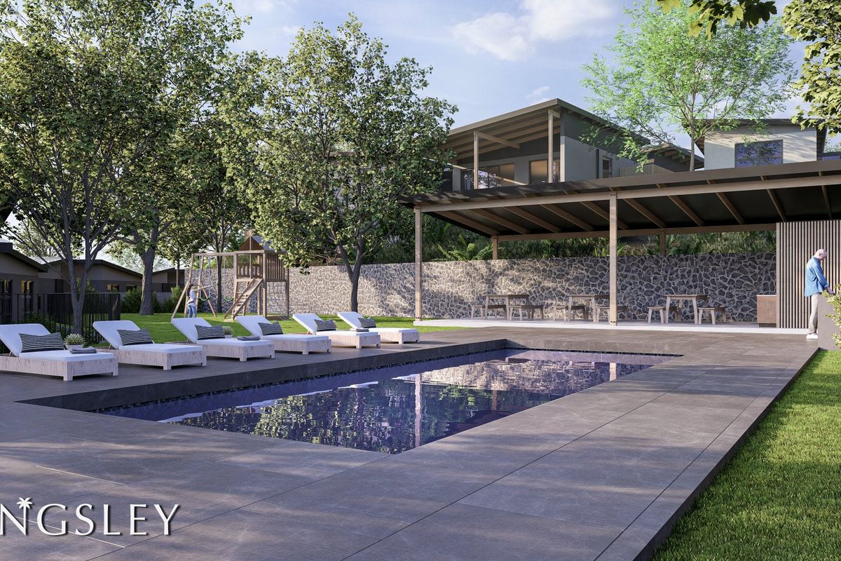 A modern outdoor pool area featuring a tiled deck, a covered patio space, and a stone retaining wall in a landscaped garden setting.