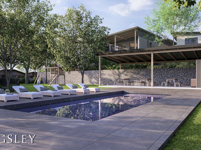 A modern outdoor pool area featuring a tiled deck, a covered patio space, and a stone retaining wall in a landscaped garden setting.