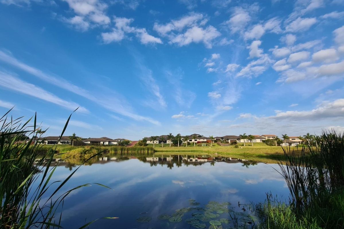 A scenic view of a tranquil lake reflecting the surrounding residential estate and blue sky.