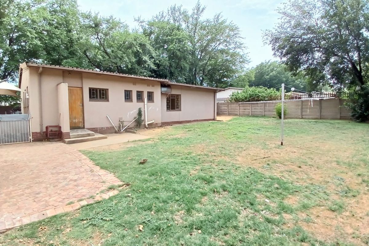 Rear view of the house featuring a paved patio area, a spacious lawn, and a perimeter boundary wall.