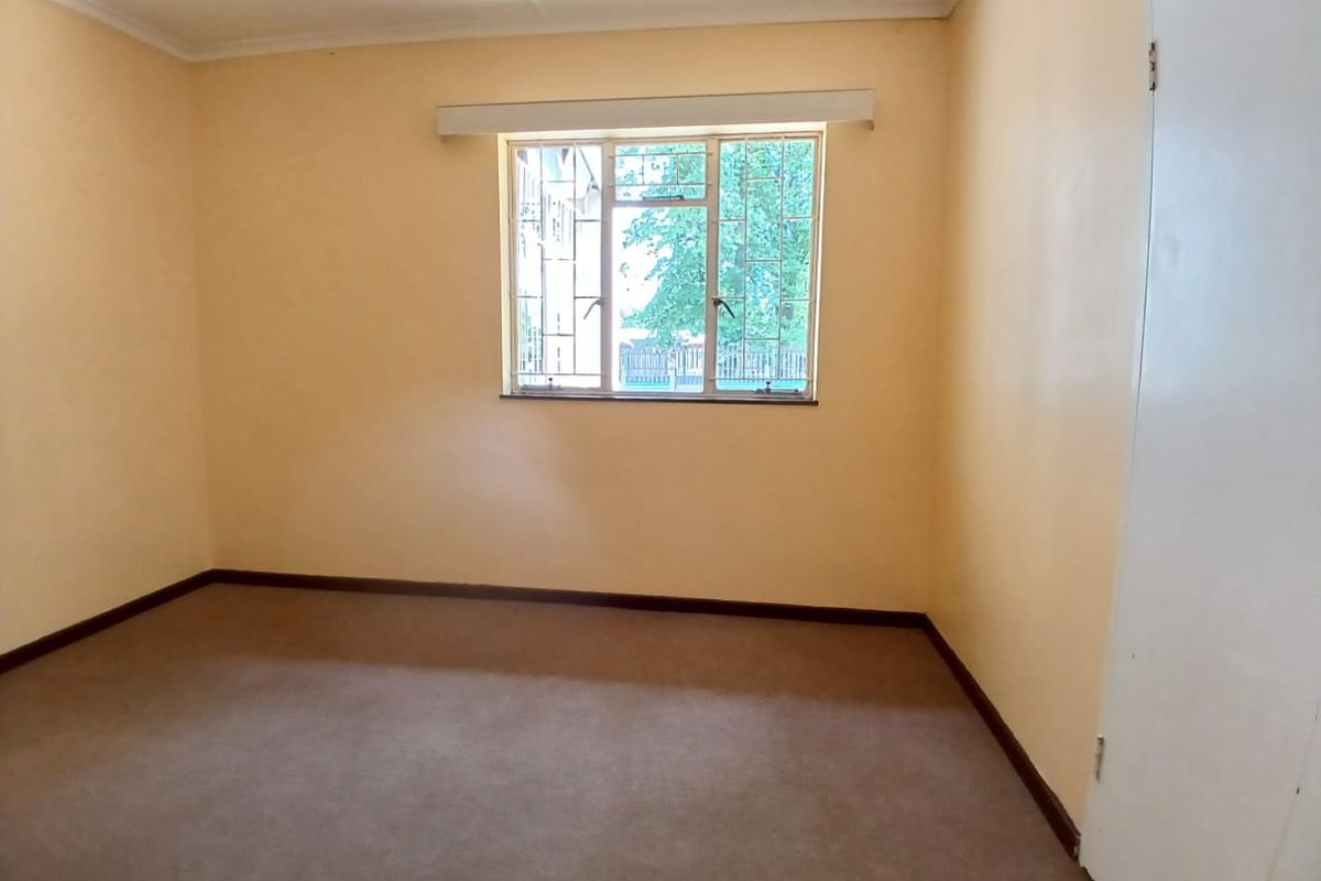 A vacant bedroom featuring neutral wall paint, carpeted flooring, and a window fitted with security bars.