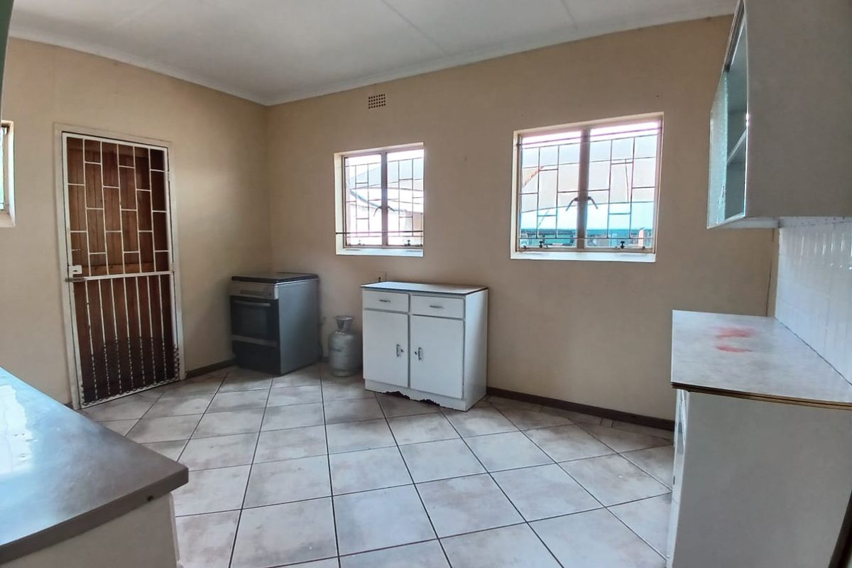 A functional kitchen space featuring tiled flooring, built-in cabinetry, and security bars on windows and doors, offering a blank canvas for renovation.