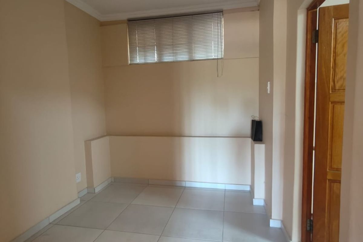 A vacant room featuring neutral wall tones, tiled flooring, a horizontal window blind, and a wooden door frame.