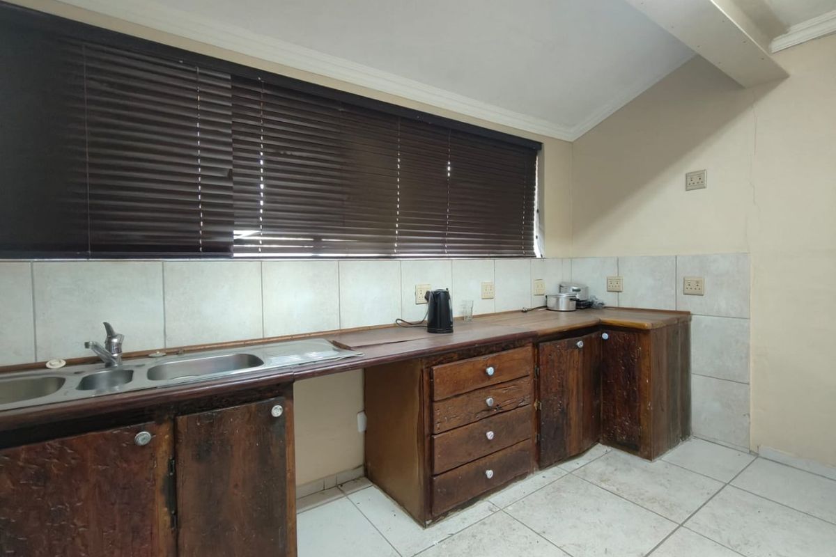 A kitchen area featuring wooden cabinetry, tiled splashbacks, a double sink, and tiled flooring, requiring cosmetic updates.