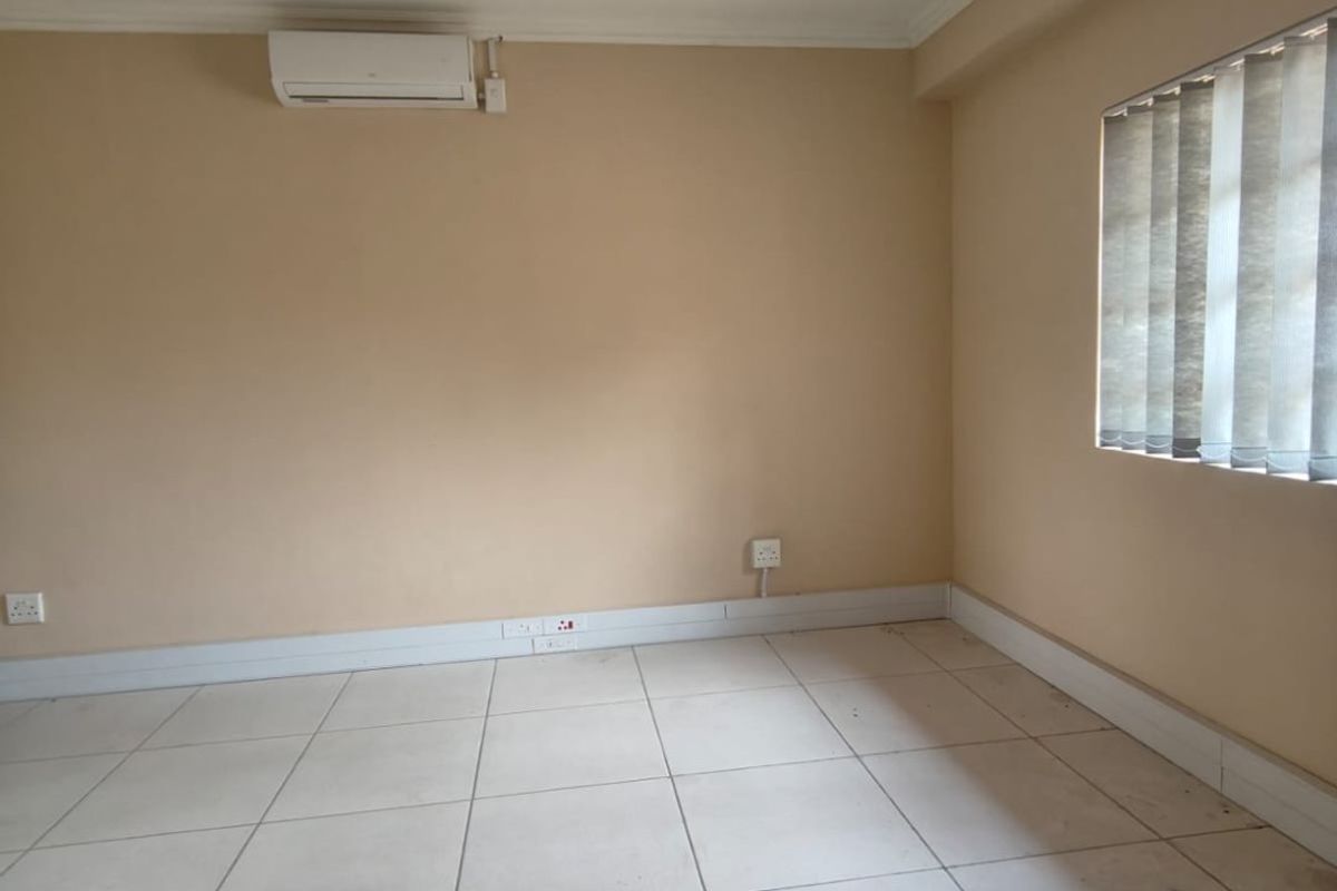 An empty room featuring tiled flooring, a wall-mounted air conditioning unit, and vertical window blinds.