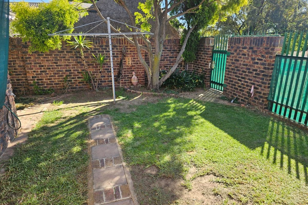 A private rear garden featuring a brick boundary wall, paved pathway, established tree, and a metal security gate.