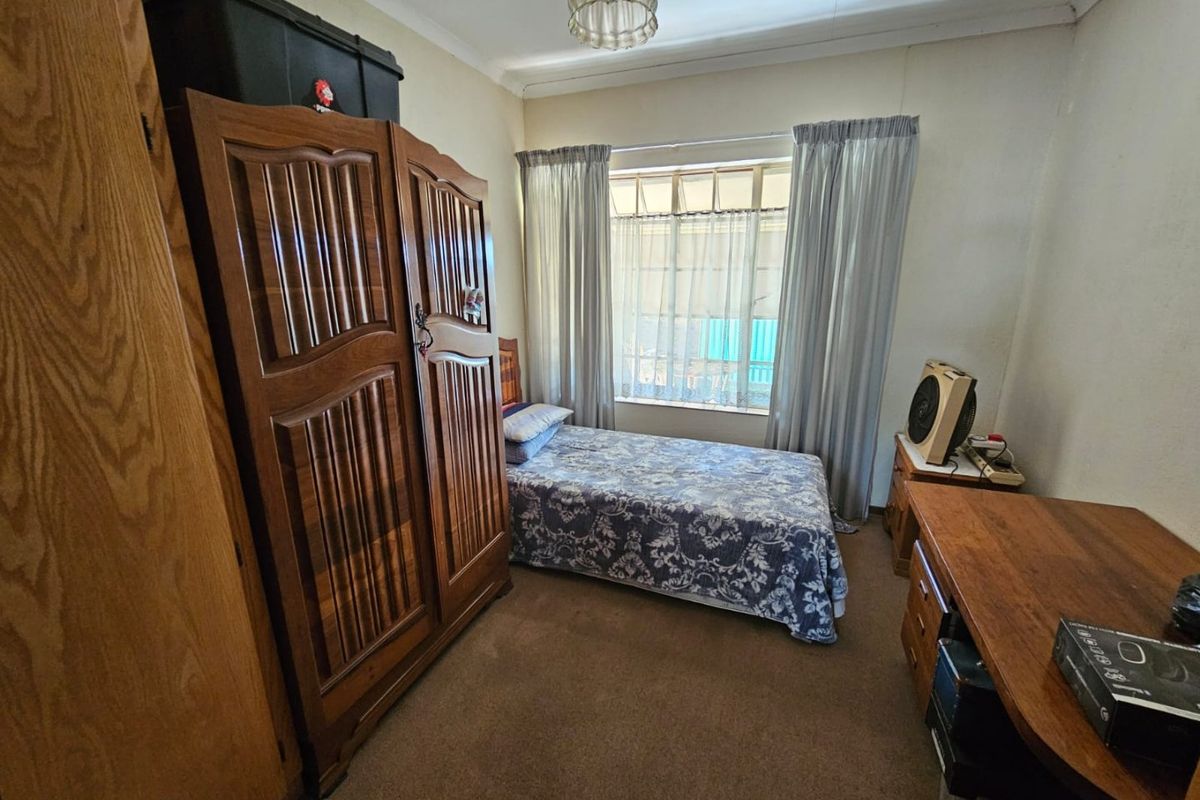 A functional bedroom featuring carpeted flooring, a large window with curtains, and built-in cupboard space.